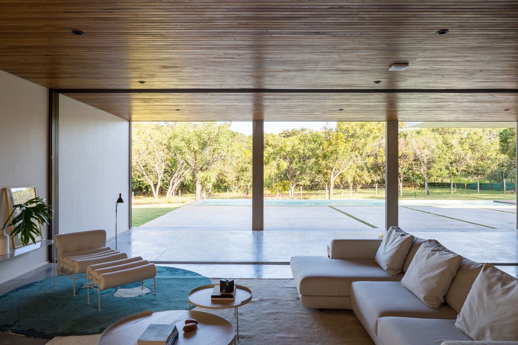 Dois volumes sobrepostos compõem esta casa de 500 m² em Brasília. Projeto de Bloco Arquitetos. Na foto, sala com poltrona, sofá e vista para o jardim.