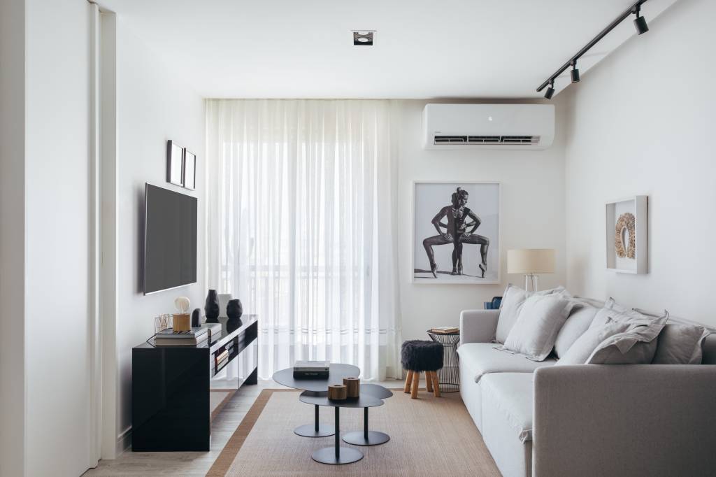 Estilo escandinavo inspira décor de apê de 84m² com paleta preta e branca. Projeto de Nilton Montarroyos. Na foto, sala de estar com sofá cinza claro, rack preto, mesa de centro preta e ar condicionado.