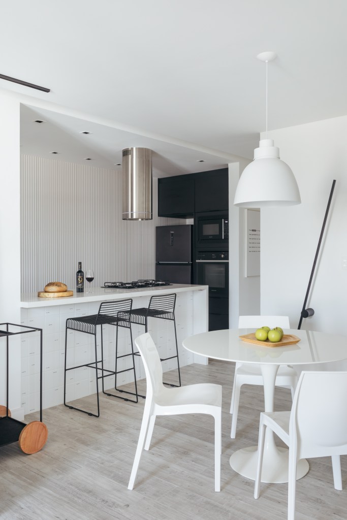 Estilo escandinavo inspira décor de apê de 84m² com paleta preta e branca. Projeto de Nilton Montarroyos. Na foto, sala de jantar integrada com cozinha minimalista, bancada branca, banquetas pretas.
