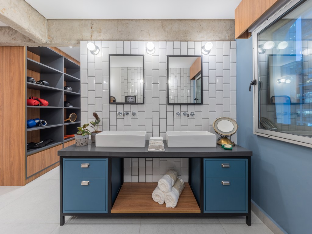 Estilo industrial e elementos clássicos se unem em apartamento de 130 m². Projeto de Pietro Terlizzi. Na foto, banheiro com pia dupla, gabinete azul e tiles na parede.