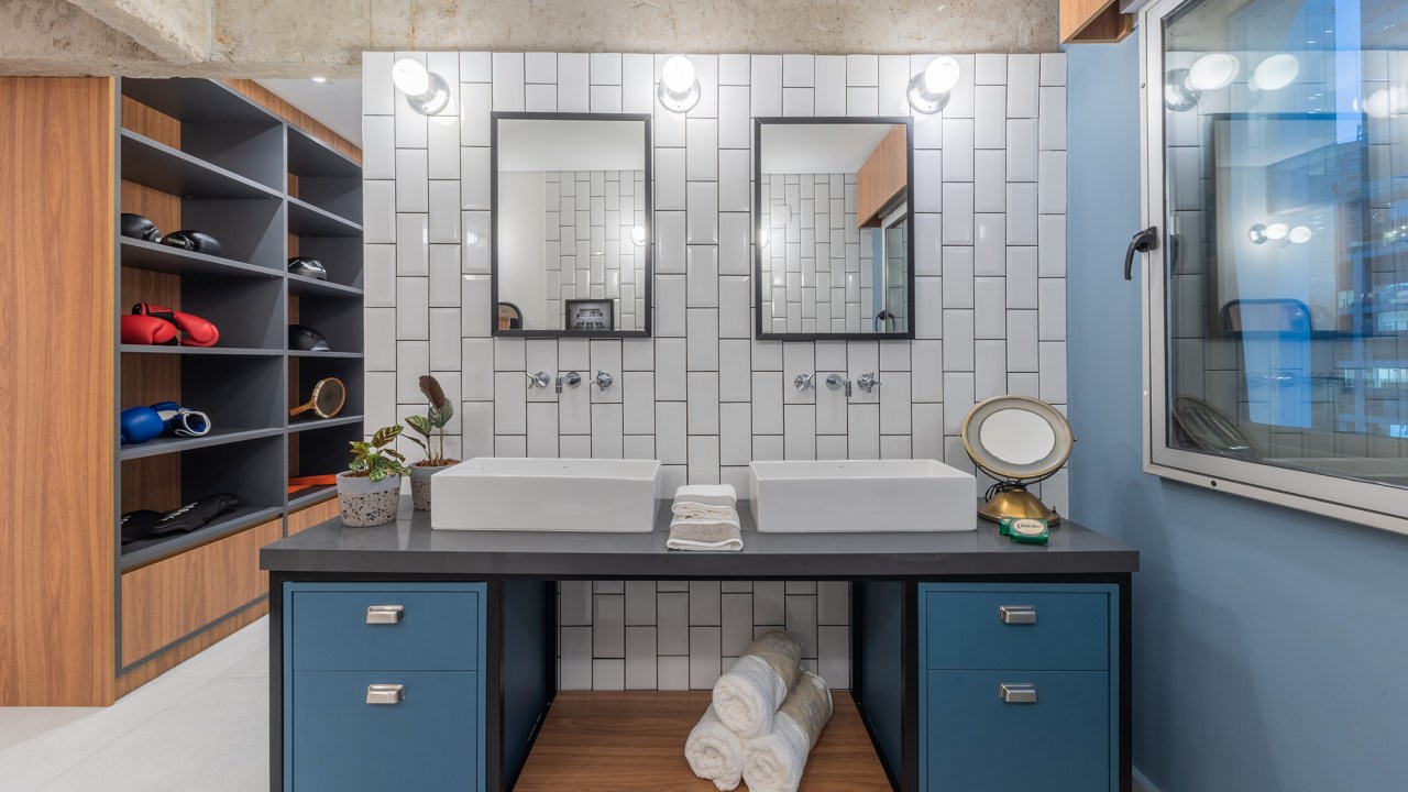Estilo industrial e elementos clássicos se unem em apartamento de 130 m². Projeto de Pietro Terlizzi. Na foto, banheiro com pia dupla, gabinete azul e tiles na parede.