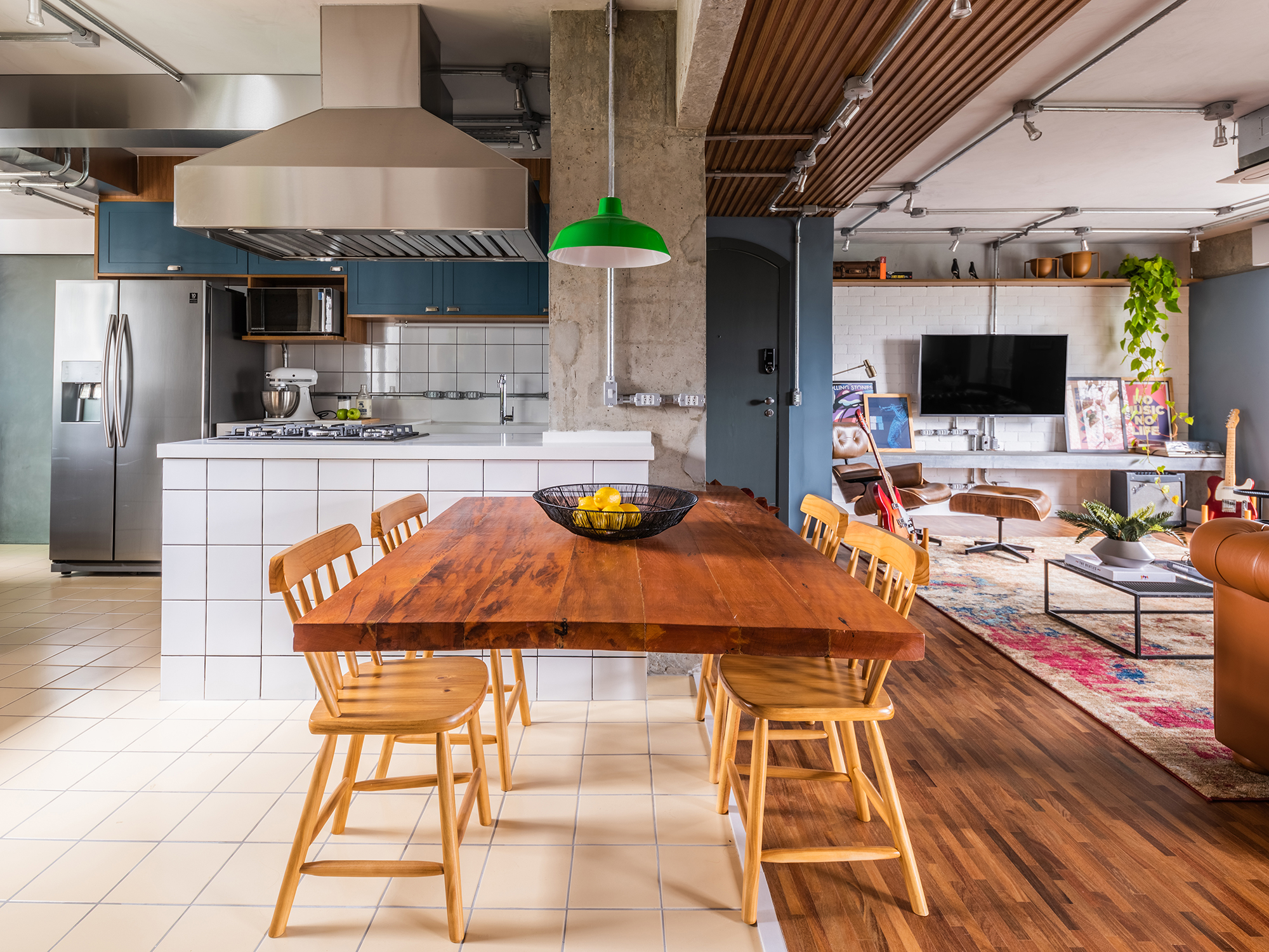 Estilo industrial e elementos clássicos se unem em apartamento de 130 m². Projeto de Pietro Terlizzi. Na foto, cozinha com marcenaria azul e tiles na parede. Sala de jantar integrada ao social.