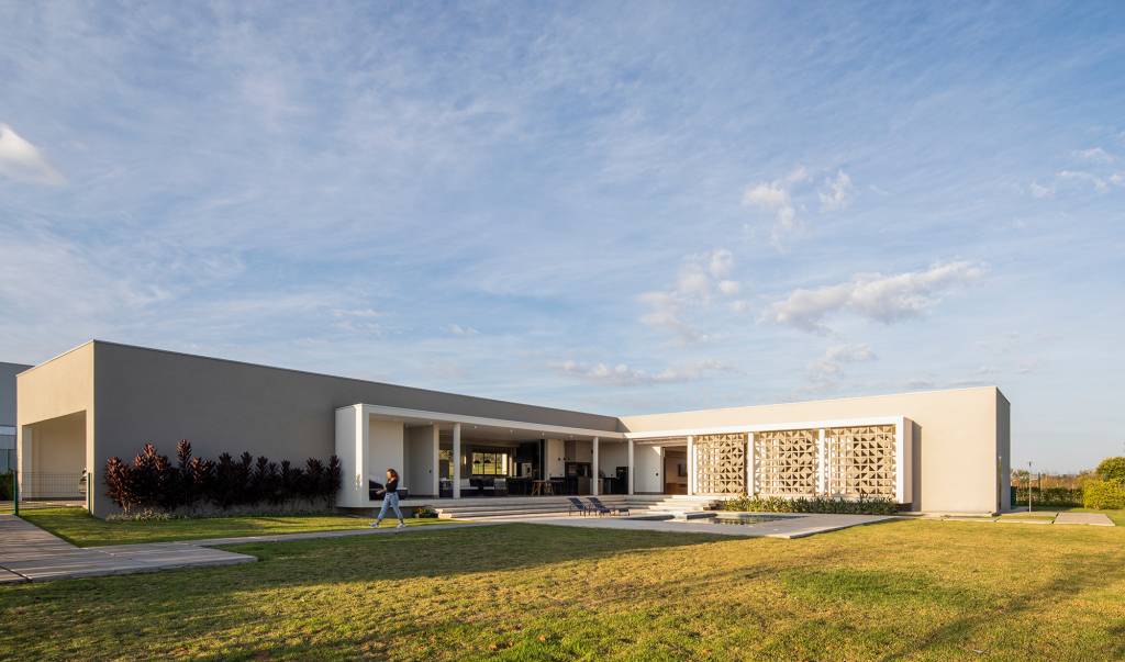 Fachada de cobogós cria efeito cênico nesta casa no interior de São Paulo. Projeto de Starq, Na foto, fachada da casa com piscina e jardim.