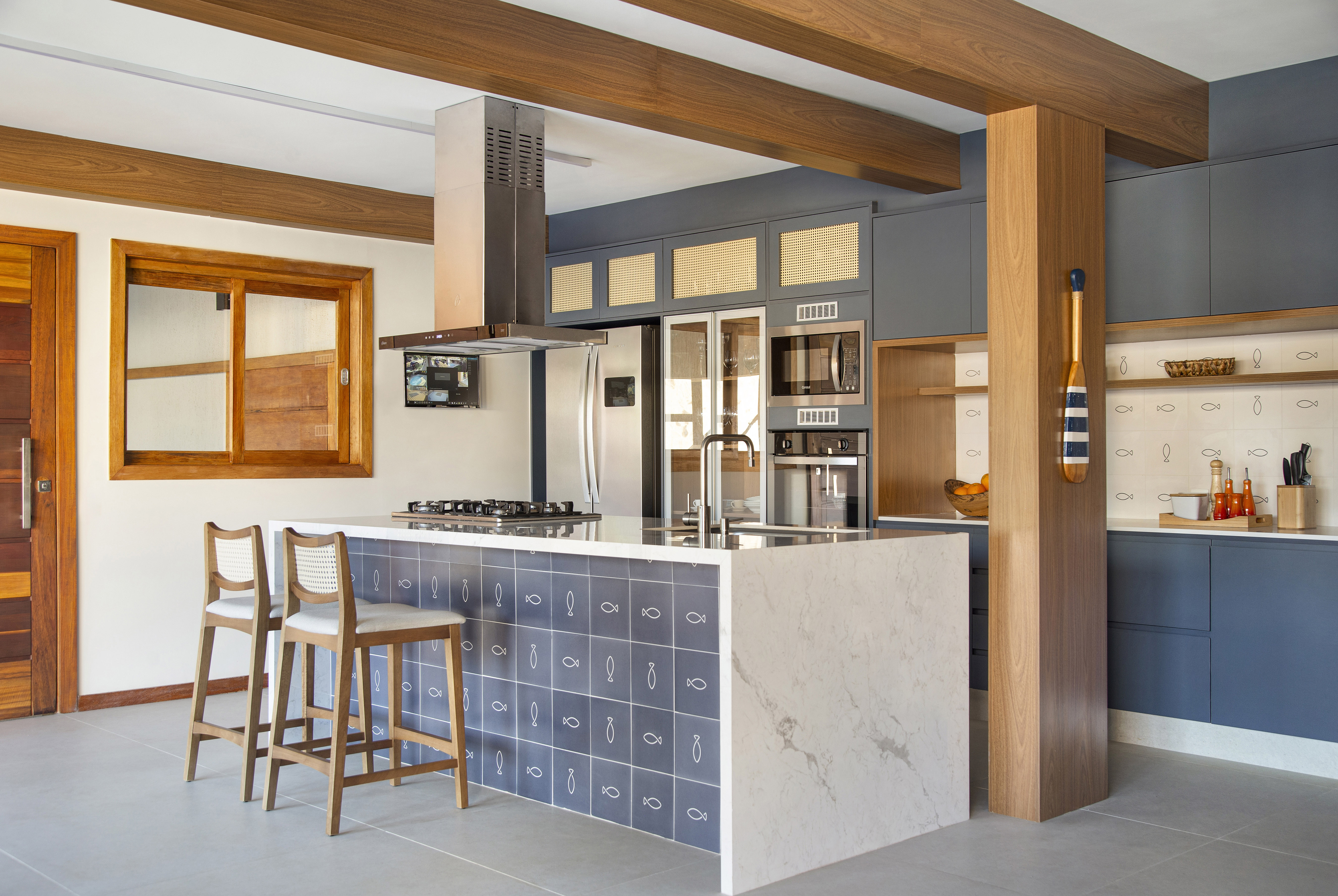 Ilha de cozinha revestida de azulejos com peixes é destaque nesta casa. Projeto de Travessa Arquitetura. Na foto, cozinha com marcenaria azul, ilha com azulejos e mármore.