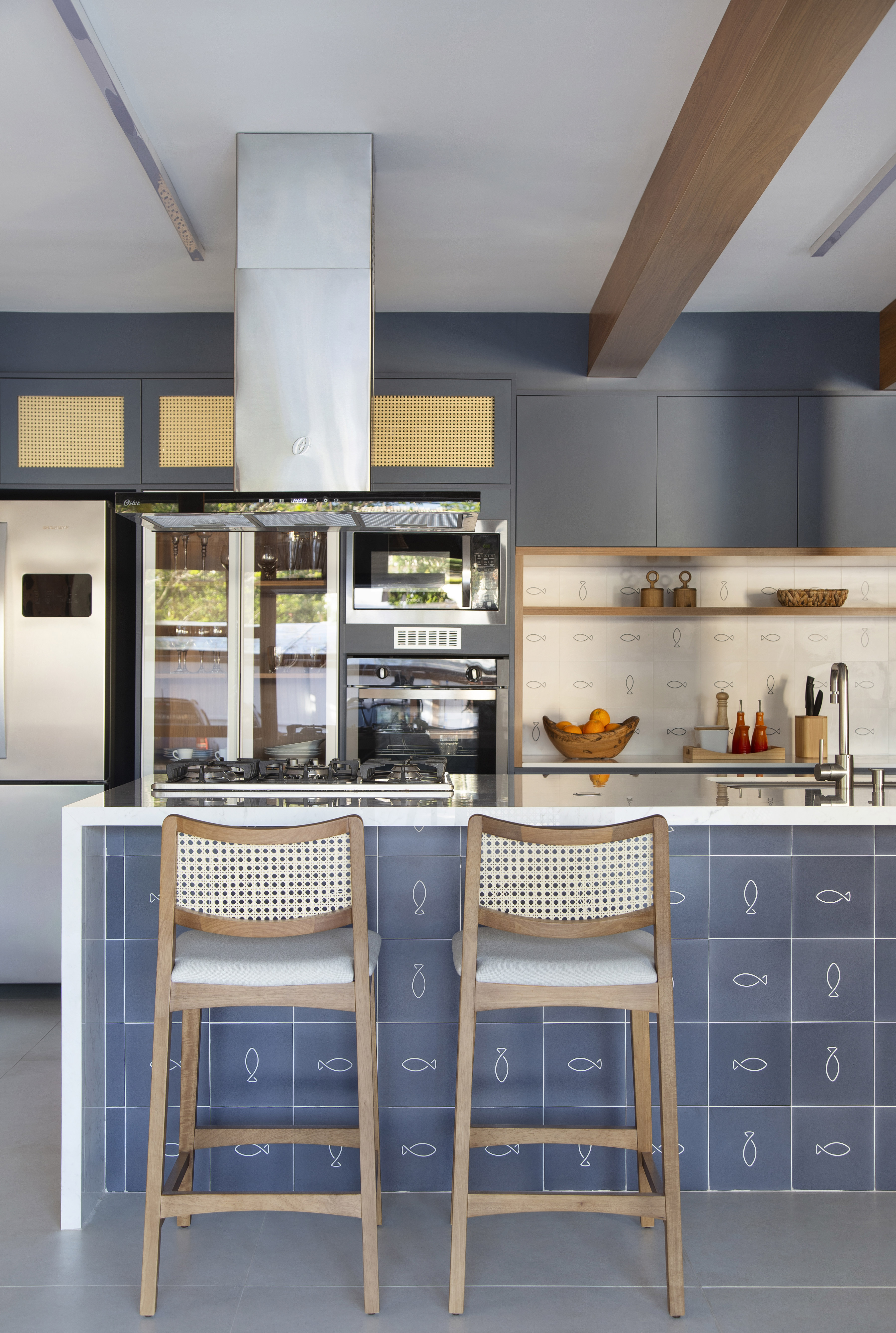 Ilha de cozinha revestida de azulejos com peixes é destaque nesta casa. Projeto de Travessa Arquitetura. Na foto, cozinha com marcenaria azul, ilha com azulejos e mármore.