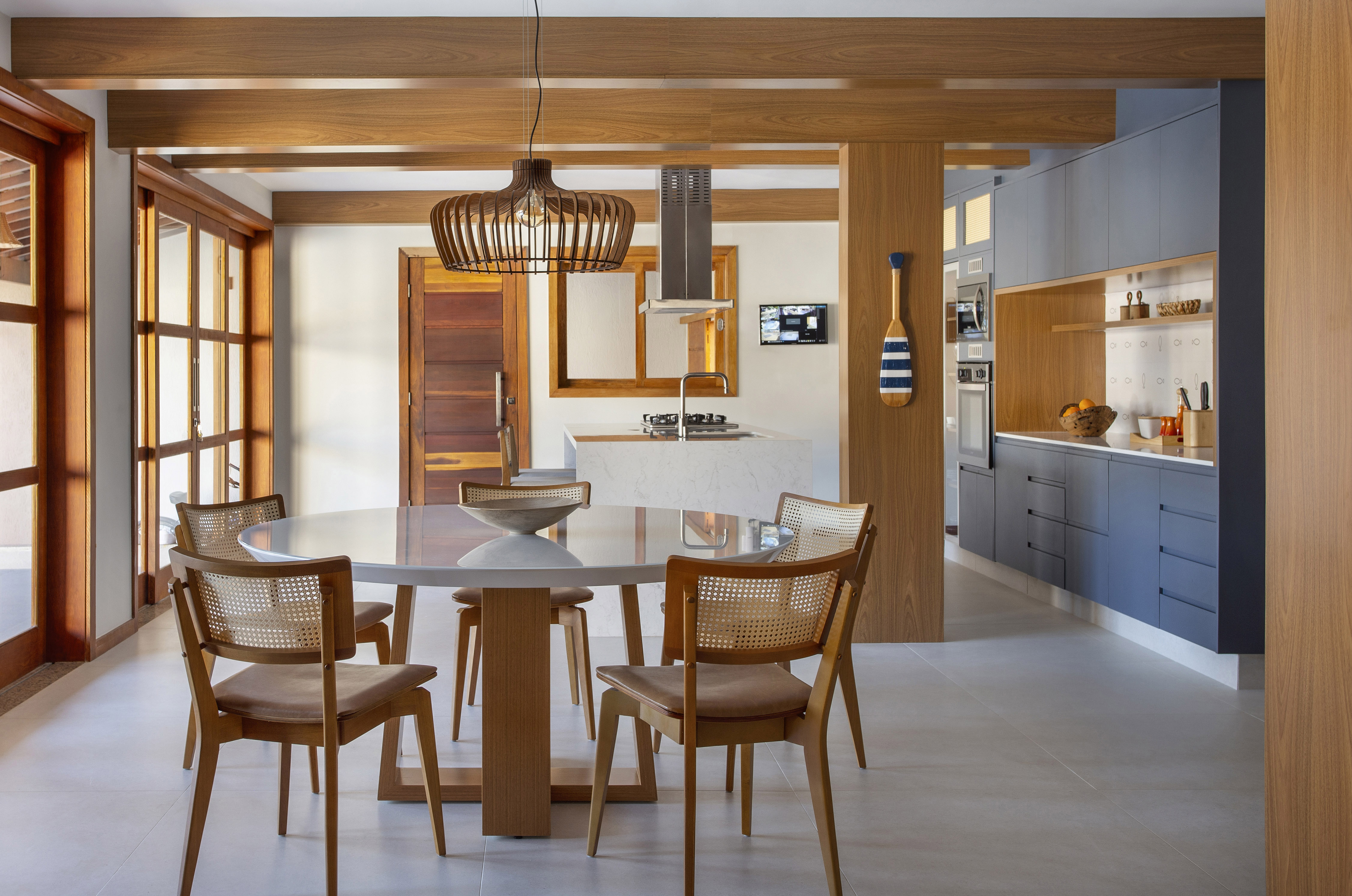 Ilha de cozinha revestida de azulejos com peixes é destaque nesta casa. Projeto de Travessa Arquitetura. Na foto, sala de jantar integrada com cozinha, luminária de palhinha, armários azuis.