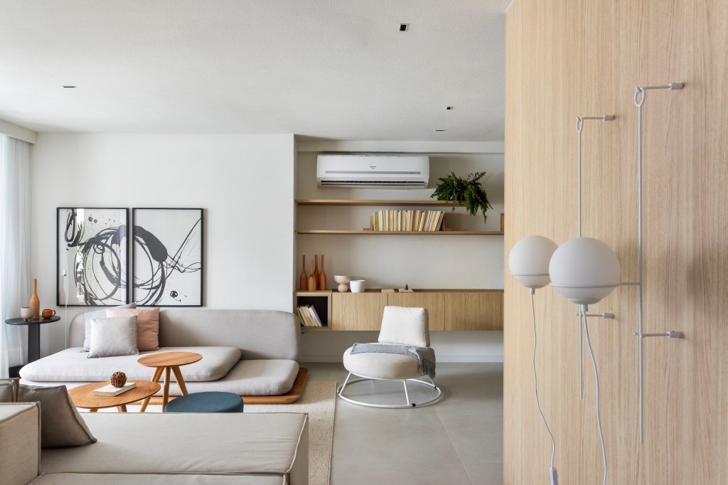 Japandi: apê de 110 m² tem décor delicado em tons de branco, rosa e cinza. Projeto de Up3 Arquitetura. Na foto, sala minimalista com sofá branco, parede revestida de madeira clara, poltrona baixa cinza.