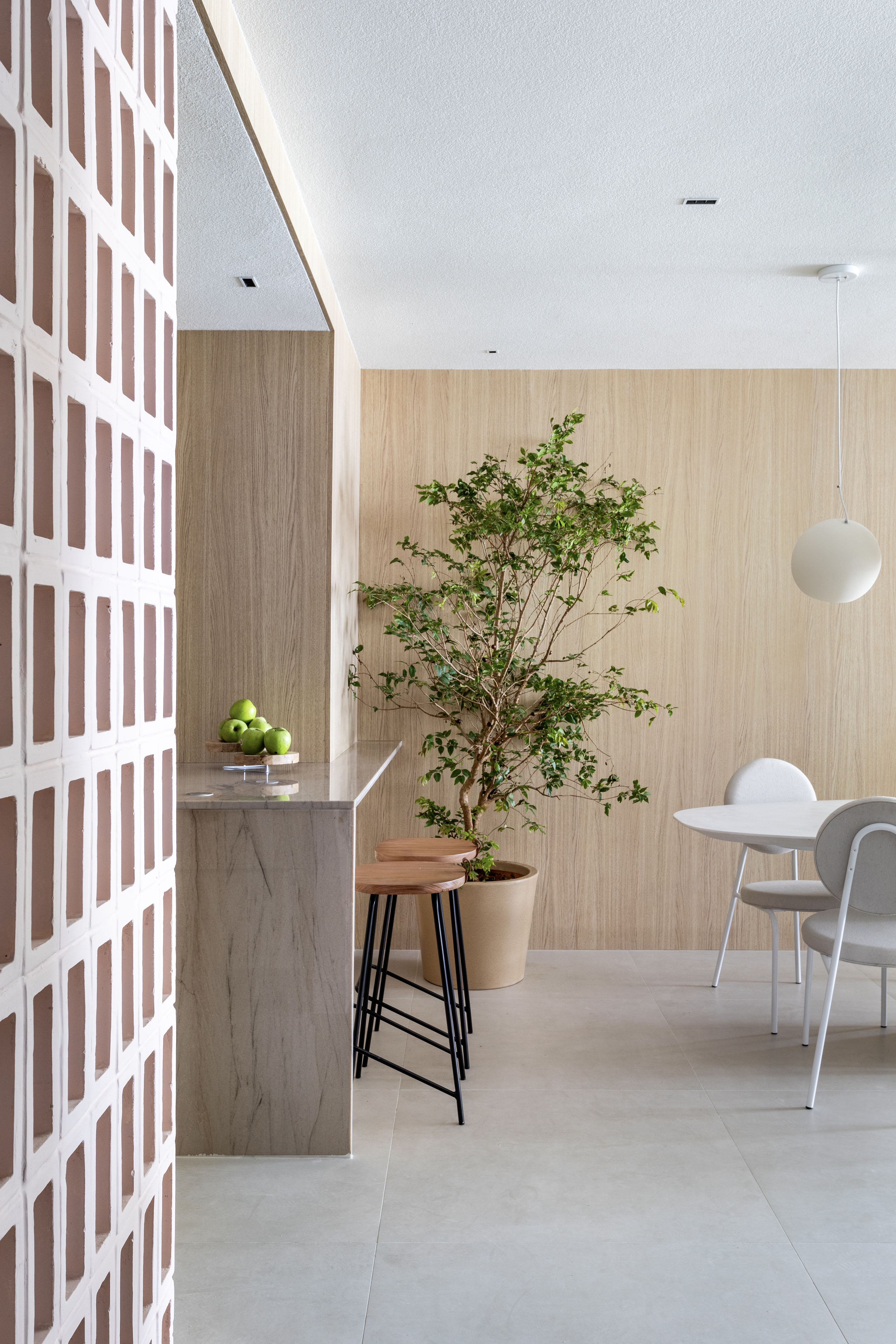 Japandi: apê de 110 m² tem décor delicado em tons de branco, rosa e cinza. Projeto de Up3 Arquitetura. Na foto, sala de estar minimalista, parede revestida de madeira clara, árvore.