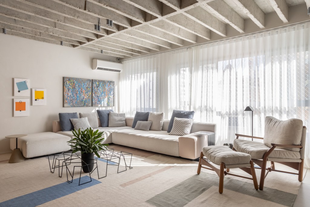 Laje de concreto, mesa em balanço e cozinha azul marcam apê de 115 m². Projeto do escritório Si Saccab. Na foto, sala com sofá em L, cortina e laje de concreto.
