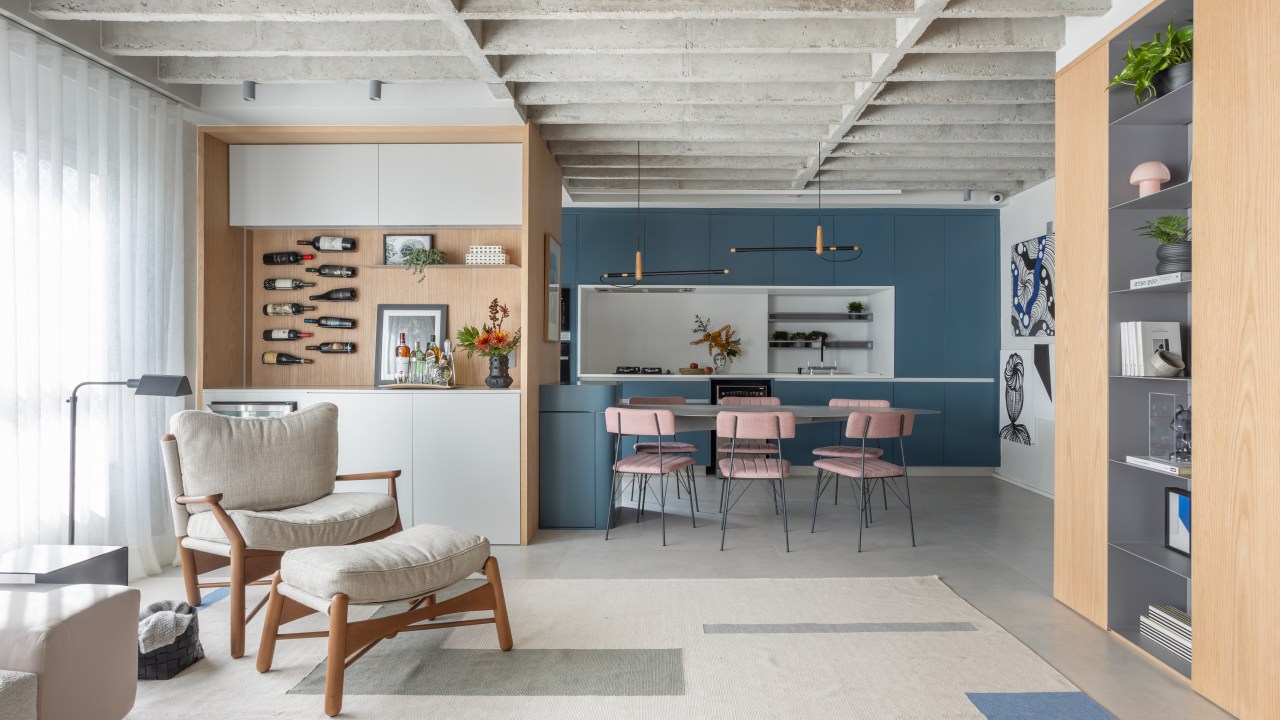 Laje de concreto, mesa em balanço e cozinha azul marcam apê de 115 m². Projeto do escritório Si Saccab. Na foto, cozinha integrada com a sala, adega, marcenaria azul e poltrona.