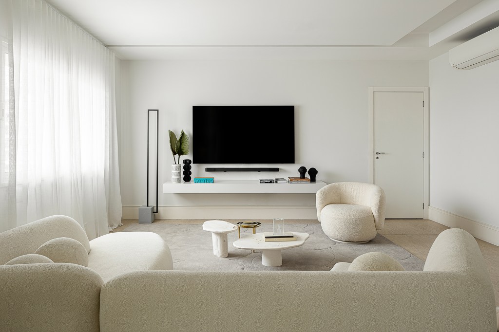 Linhas orgânicas e mobiliário solto compõem décor de apê alugado de 240 m². Projeto de Dubal Arquitetura. Na foto, sala de estar e tv com sofá curvo e poltrona.