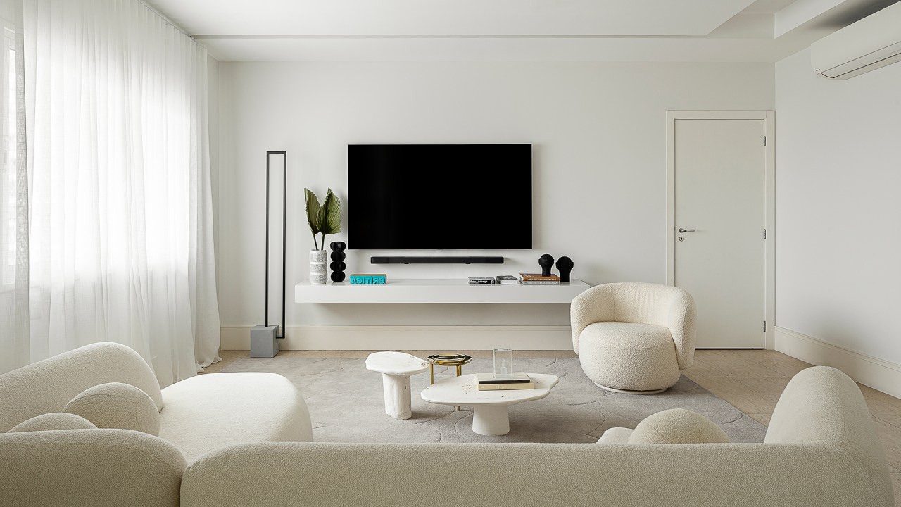 Linhas orgânicas e mobiliário solto compõem décor de apê alugado de 240 m². Projeto de Dubal Arquitetura. Na foto, sala de estar e tv com sofá curvo e poltrona.
