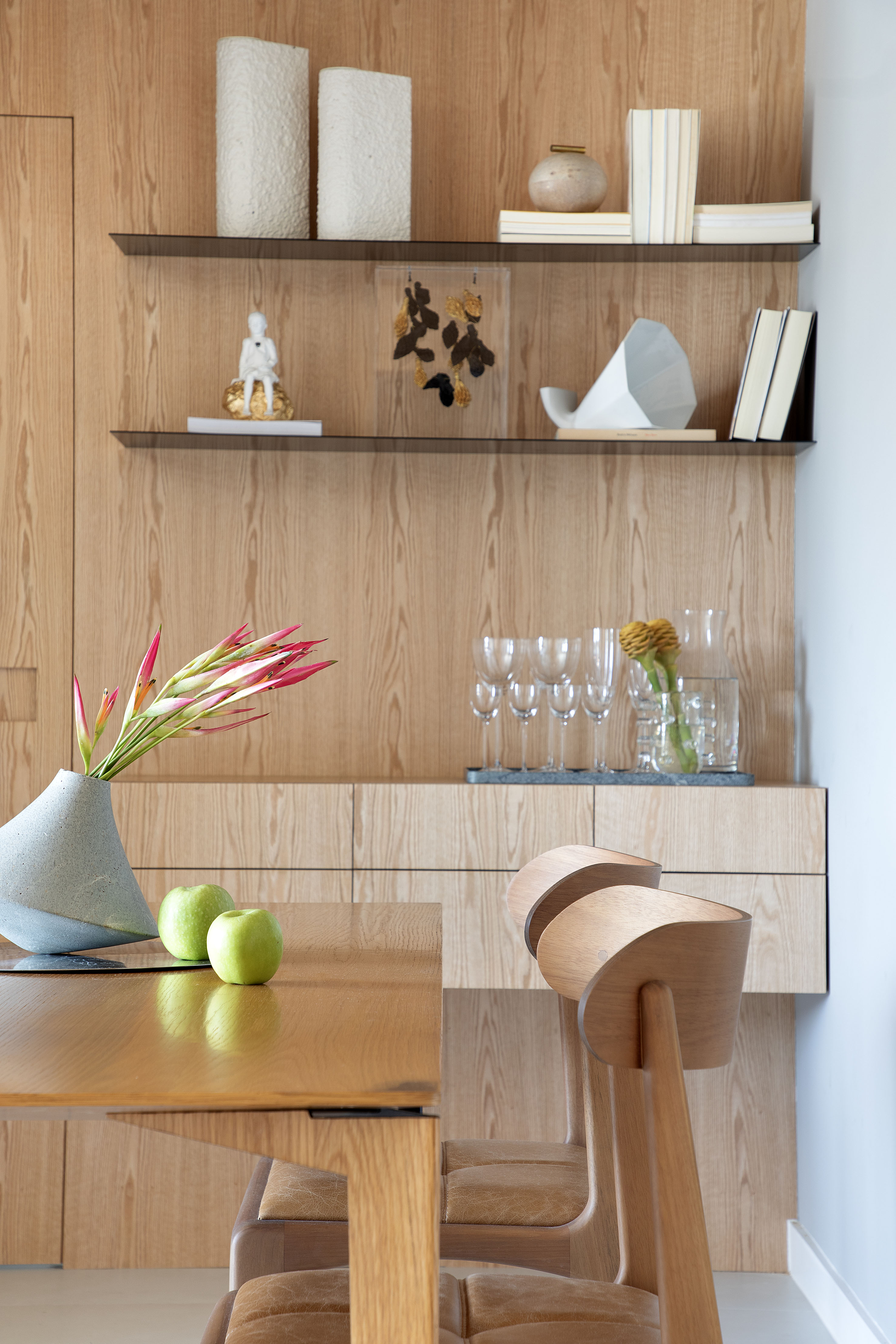 Materiais naturais como madeira, couro, linho e fibra natural marcam apê. Projeto de Ikeda Arquitetura. Na foto, sala de jantar com paredes revestidas de madeira, prateleiras.