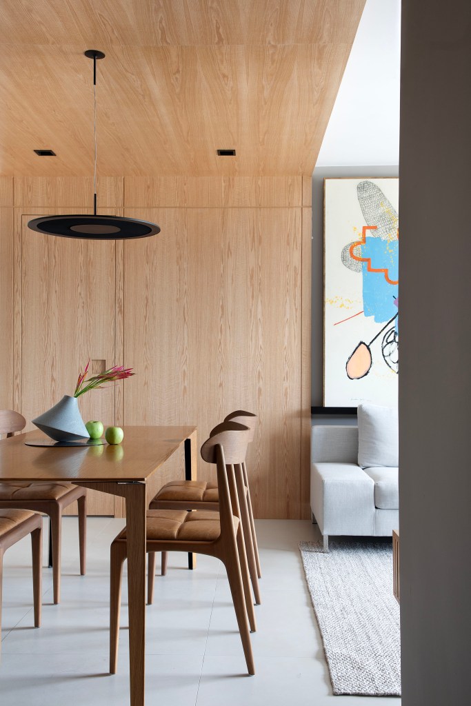 Materiais naturais como madeira, couro, linho e fibra natural marcam apê. Projeto de Ikeda Arquitetura. Na foto, sala de jantar com pórtico de madeira, mesa de madeira e sofá cinza.