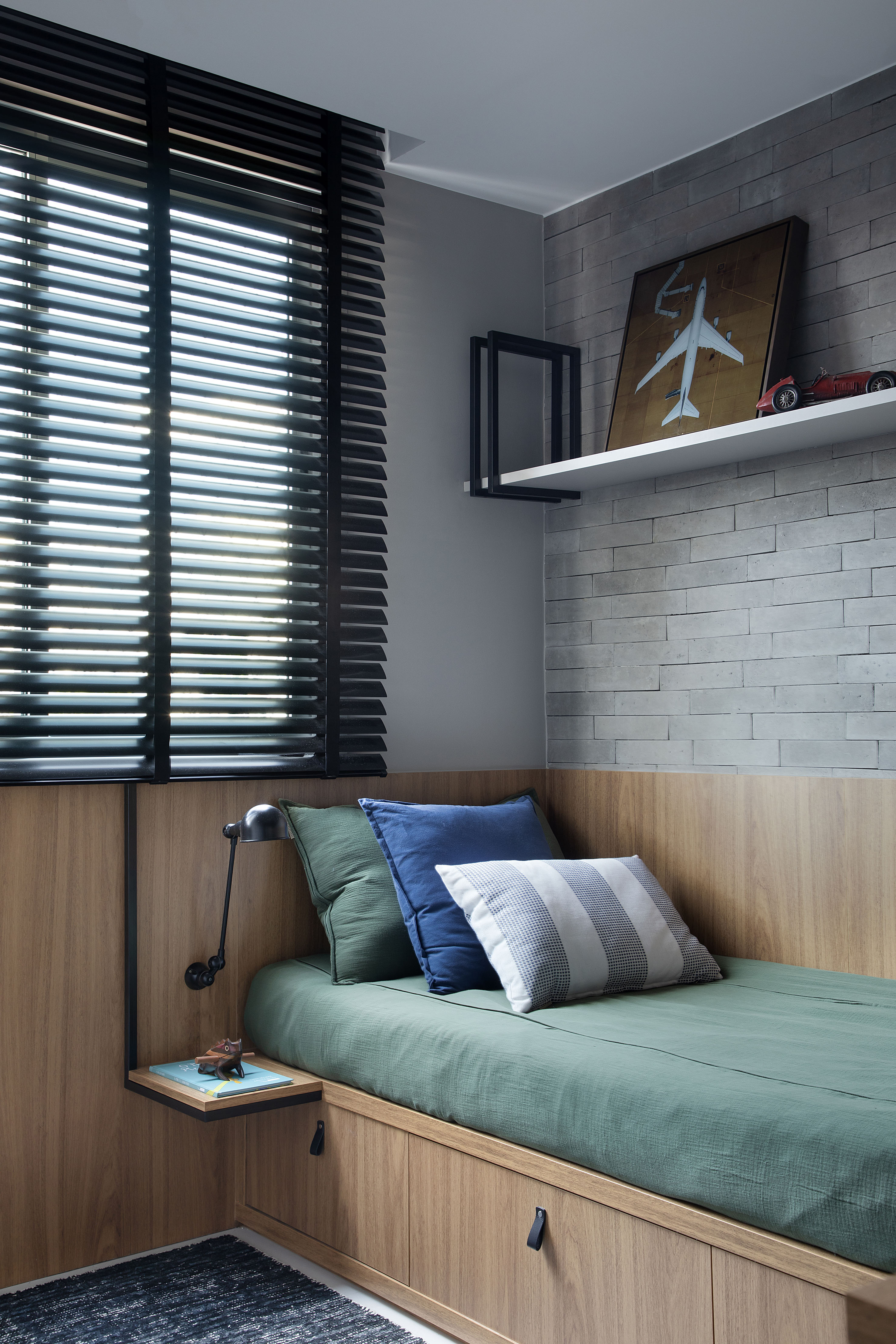 Materiais naturais como madeira, couro, linho e fibra natural marcam apê. Projeto de Ikeda Arquitetura. Na foto, quarto infantil com cama de solteiro, parede de tijolinhos e persiana.