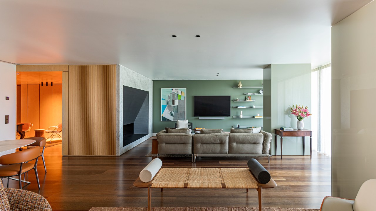 Mix entre antigo e moderno com diferentes culturas define apê de 290 m². Projeto de Andrea Chicharo Arquitetura. Na foto, sala de estar, tv, parede verde, sofá, prateleiras.