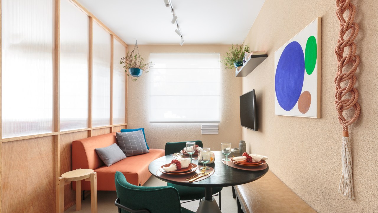 Painel translúcido e banco como rack otimizam o espaço em apê de 24 m². Projeto de Pro.a Arquitetos, Na foto, sala com sofá laranja e canto alemão,