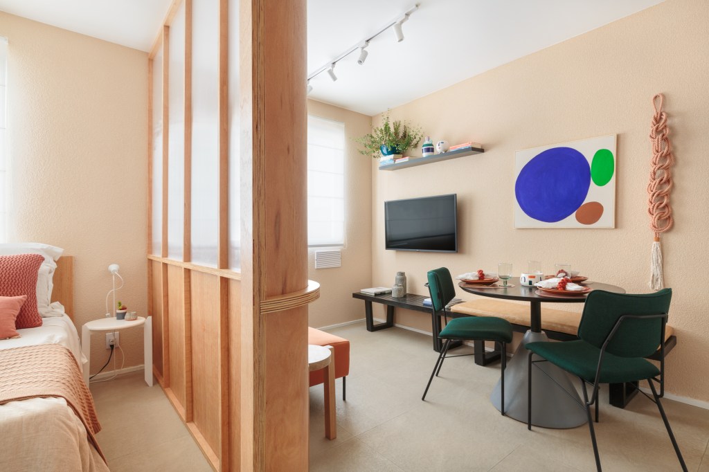 Painel translúcido e banco como rack otimizam o espaço em apê de 24 m². Projeto de Pro.a Arquitetos, Na foto, sala com sofá laranja e painel translúcido. Cozinha e sala de jantar,