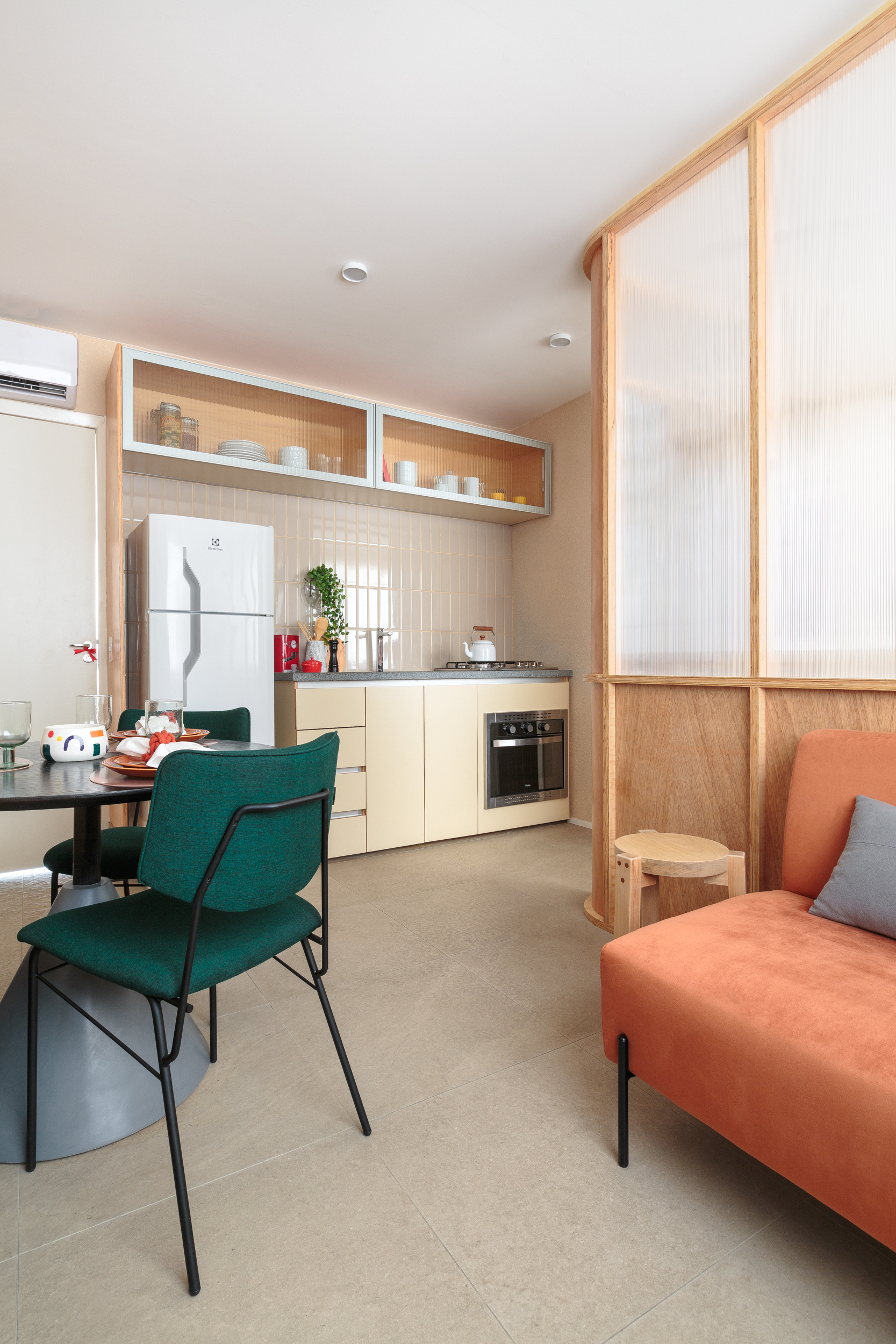 Painel translúcido e banco como rack otimizam o espaço em apê de 24 m². Projeto de Pro.a Arquitetos, Na foto, sala com sofá laranja e painel translúcido. Cozinha e sala de jantar,