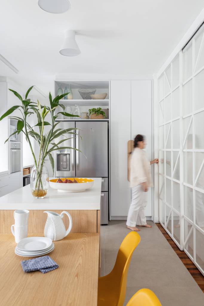 Com paleta branca, apê de 240 m² tem porta de correr inspirada em biombos. Projeto de Lucia Manzano. Na foto, cozinha minimalista branca, bancada, porta de correr de vidro.