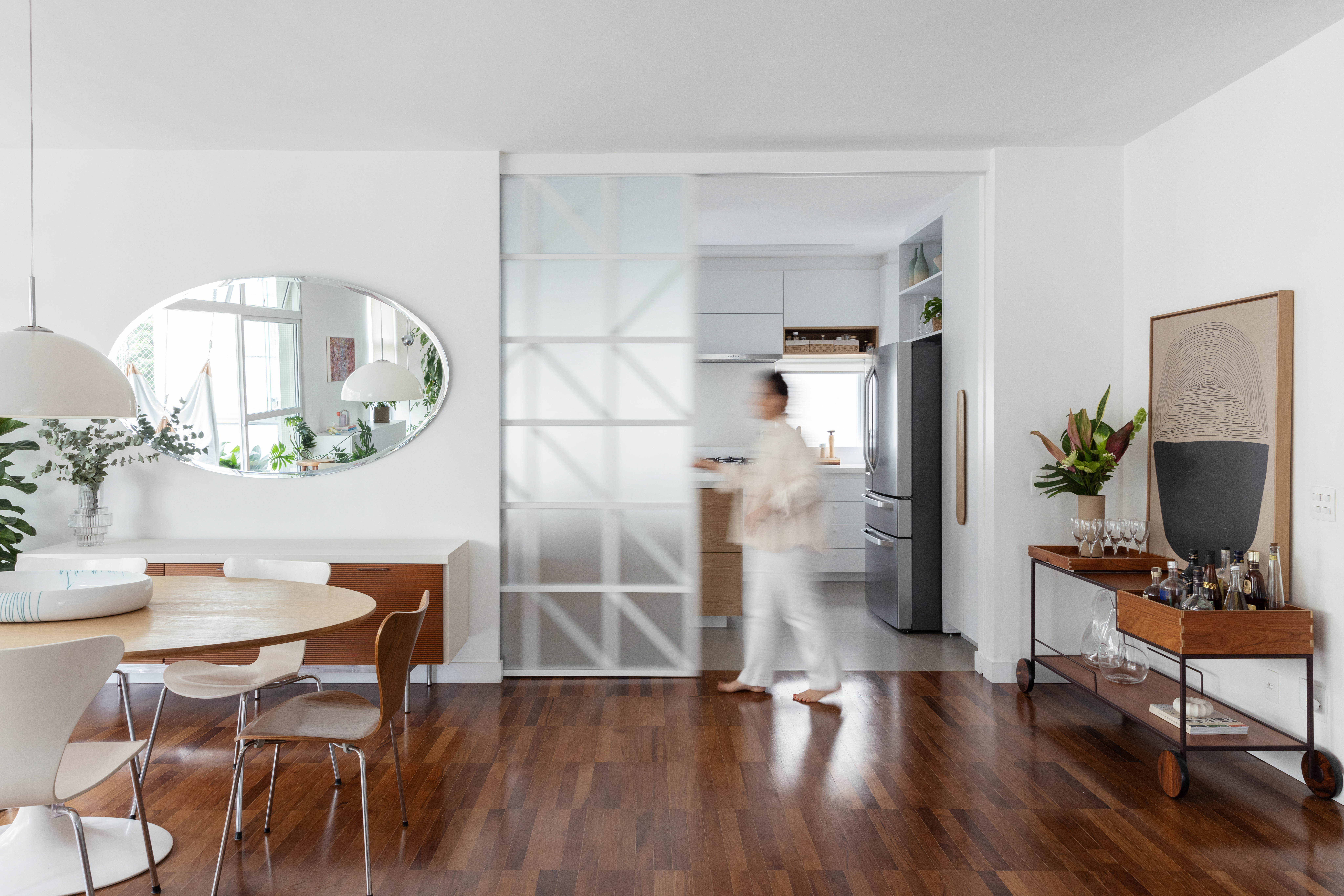 Com paleta branca, apê de 240 m² tem porta de correr inspirada em biombos. Projeto de Lucia Manzano. Na foto, sala, piso de madeira, porta de vidro de correr.