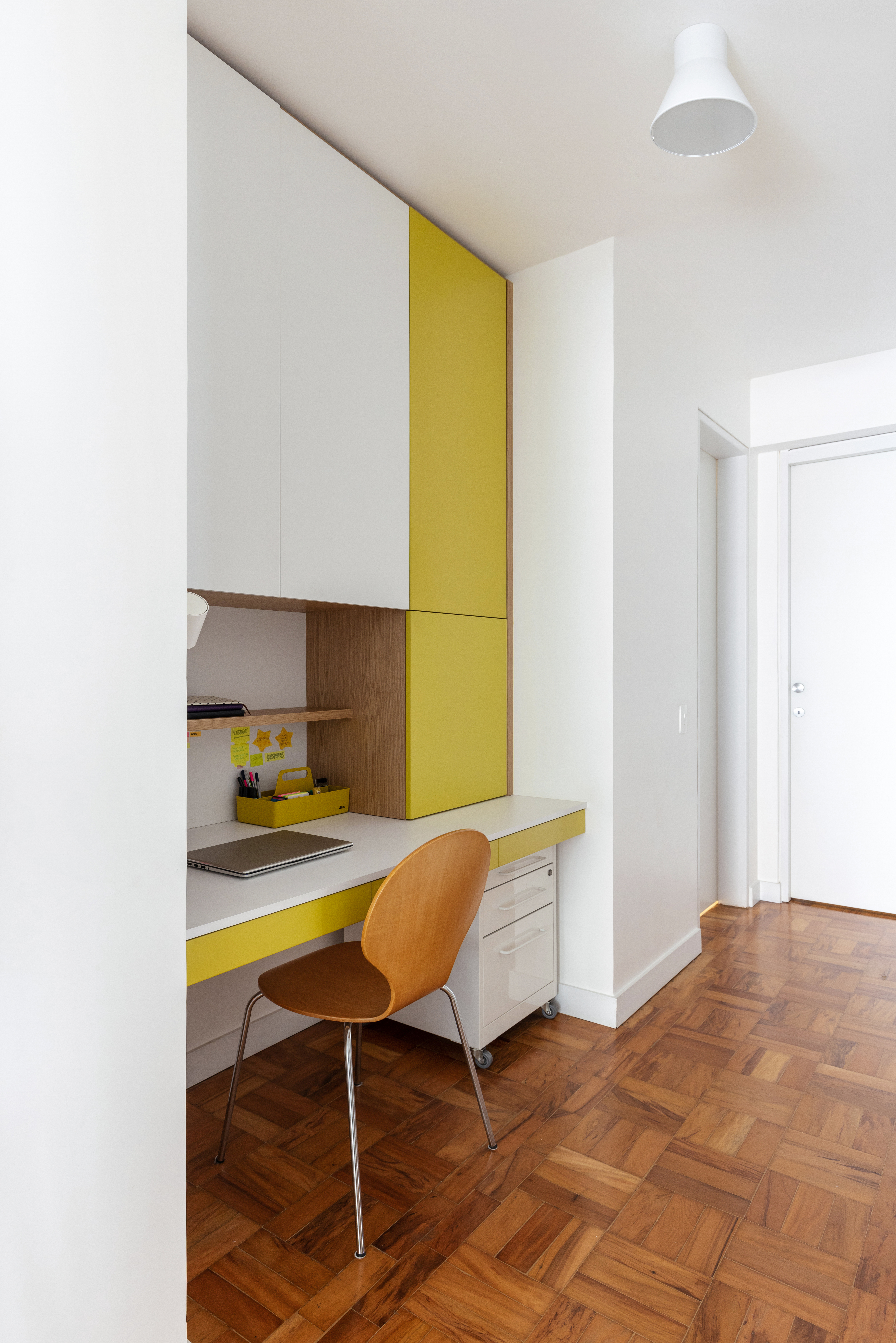 Com paleta branca, apê de 240 m² tem porta de correr inspirada em biombos. Projeto de Lucia Manzano. Na foto, home office, marcenaria branca e amarela.