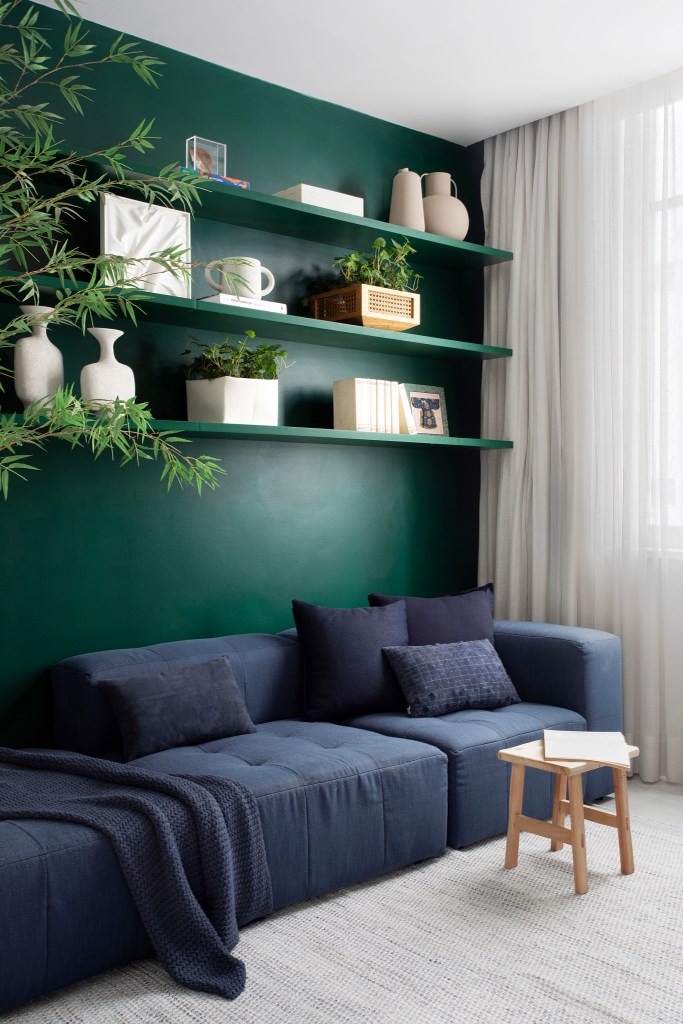 Com paleta sóbria, cobertura ganha cozinha cinza e sala íntima. Projeto de Travessa Arquitetura. Na foto, sala íntima com parede verde e sofá baixo azul marinho.