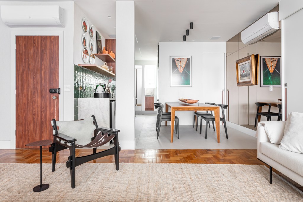 Peças afetivas com memória, design e madeira escura compõem apê de 116 m². Projeto de NOP Arquitetura. Na foto, sala de estar integrada com jantar, tapete bege, mesa de madeira.