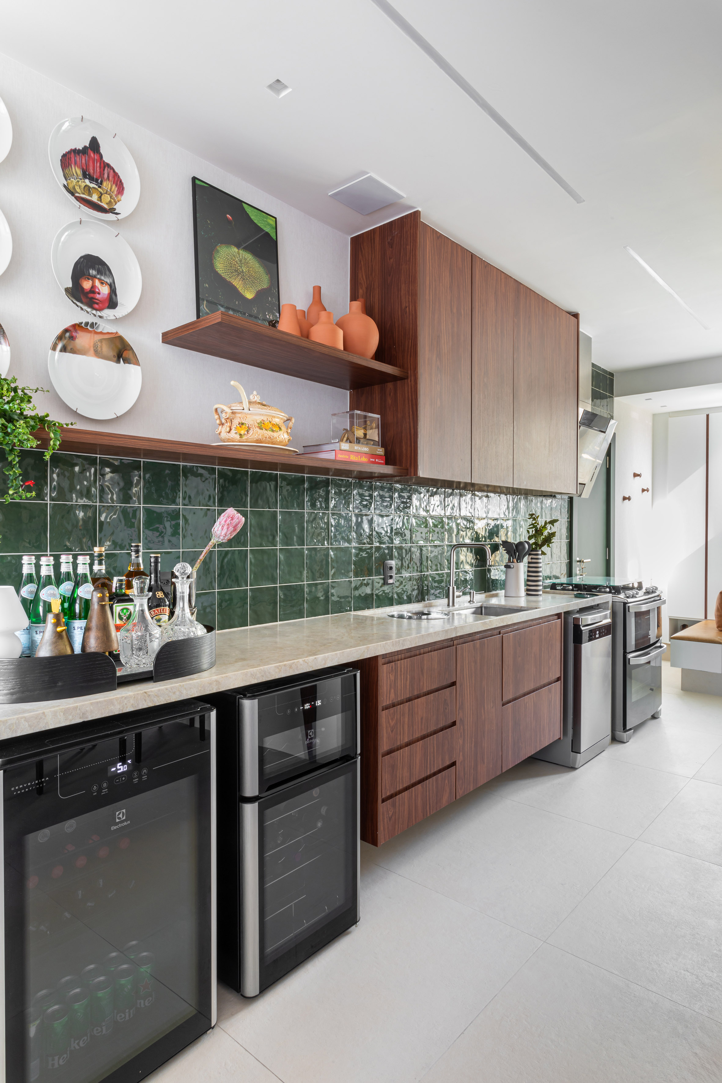 Peças afetivas com memória, design e madeira escura compõem apê de 116 m². Projeto de NOP Arquitetura. Na foto, cozinha com azulejos verdes, pratos na parede e prateleira com planta.