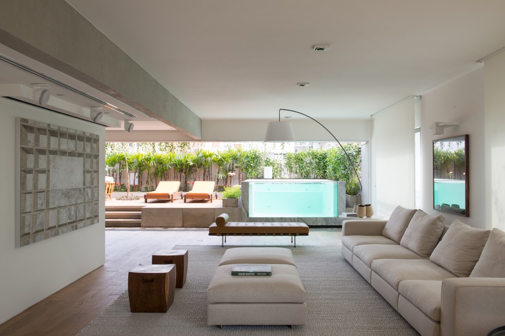 Piscina transparente parece estar dentro da sala neste apê de 400 m². Projeto de Alexandre Del Fabbro. Na foto, sala de estar com vista para a varanda com piscina.