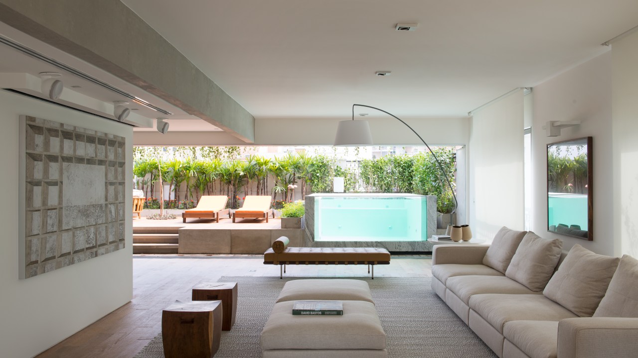 Piscina transparente parece estar dentro da sala neste apê de 400 m². Projeto de Alexandre Del Fabbro. Na foto, sala de estar com vista para a varanda com piscina.