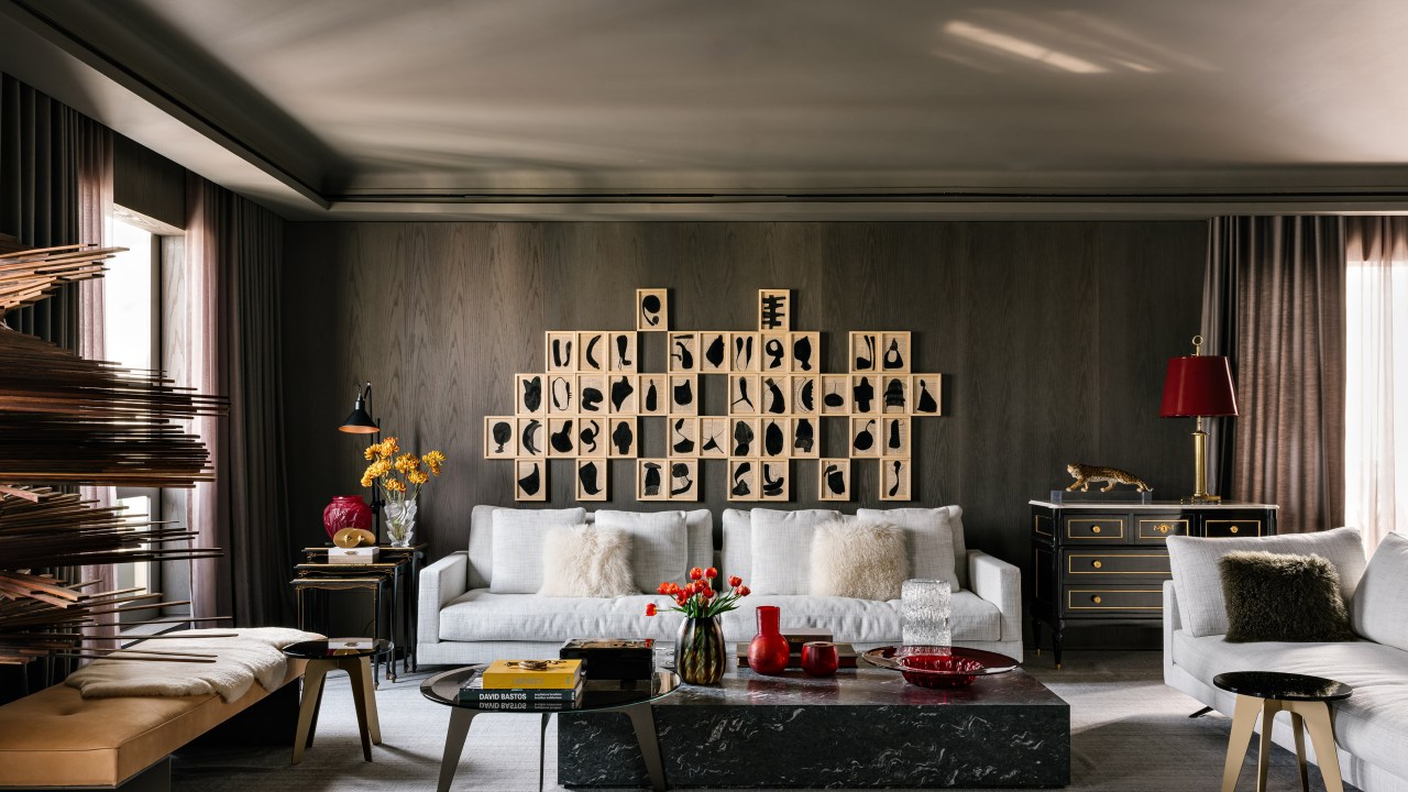 Piso de mármore e parede com painéis escuros dão elegância sóbria a apê. Projeto de DB Arquitetos. Na foto, sala de estar com paredes revestidas de madeira escura, mesa de centro, sofá branco.