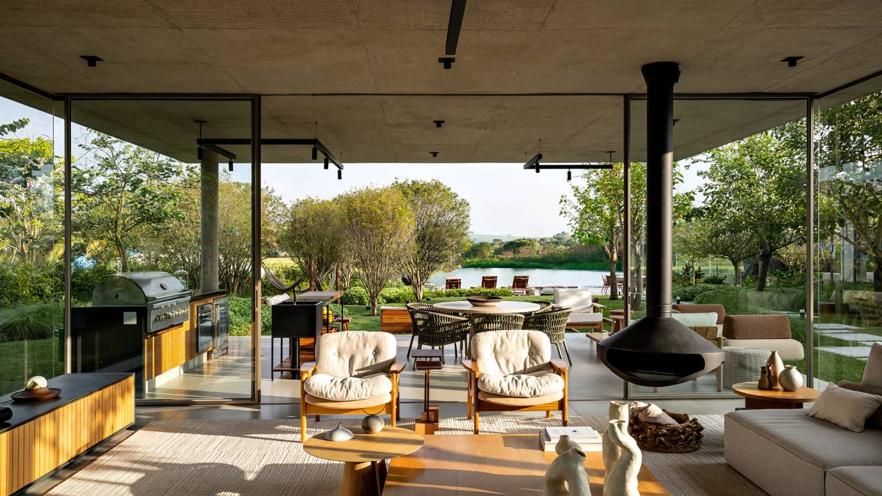 Placas de cobre oxidado e vidro integram esta casa de 653 m² à natureza, Projeto de FGMF. Na foto, sala da casa com lareira e vista para o lago.