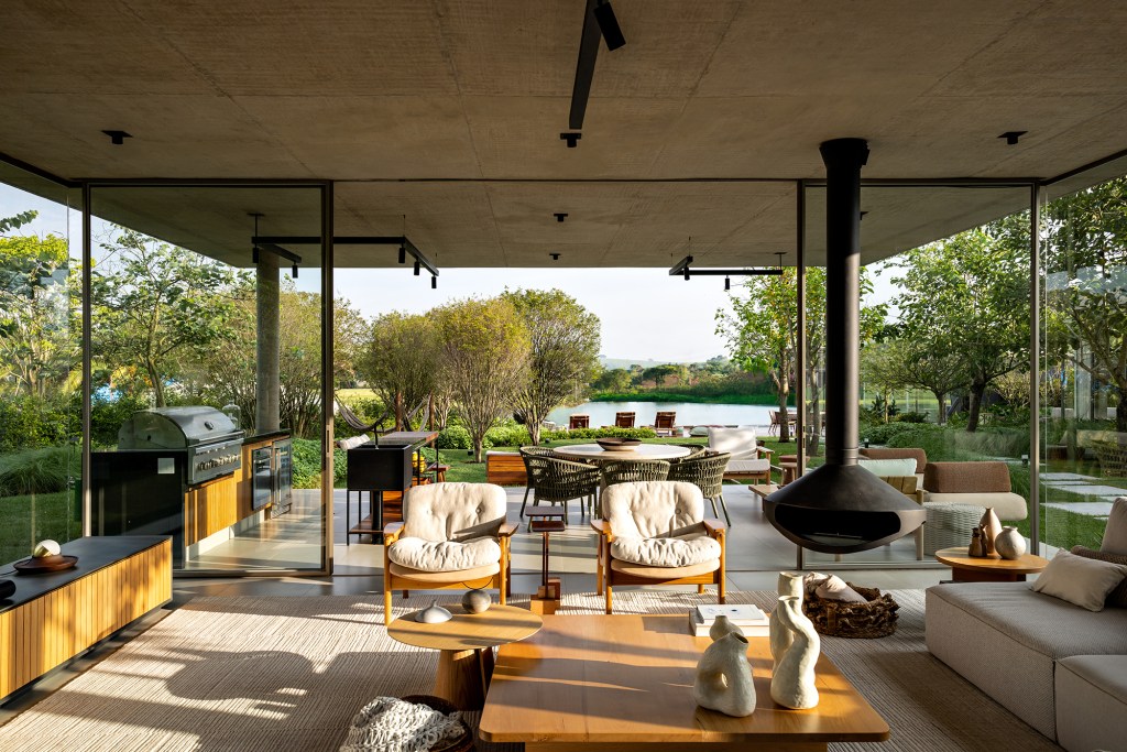 Placas de cobre oxidado e vidro integram esta casa de 653 m² à natureza, Projeto de FGMF. Na foto, sala da casa com lareira e vista para o lago.