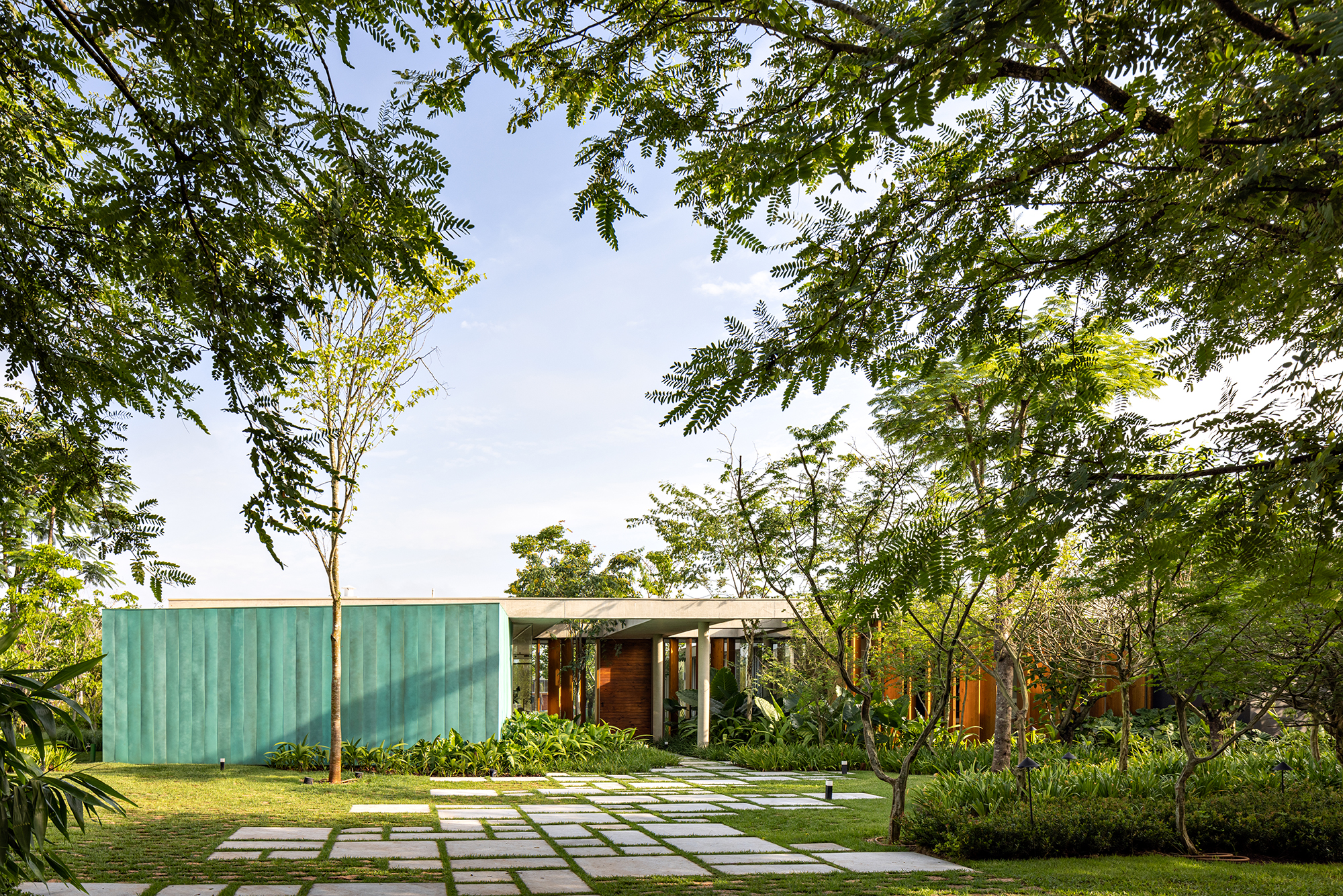 Placas de cobre oxidado e vidro integram esta casa de 653 m² à natureza, Projeto de FGMF. Na foto, fachada da casa com jardim.