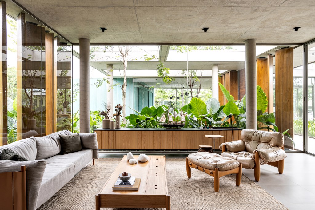 Placas de cobre oxidado e vidro integram esta casa de 653 m² à natureza, Projeto de FGMF. Na foto, sala de estar com aparador e vista para o jardim.