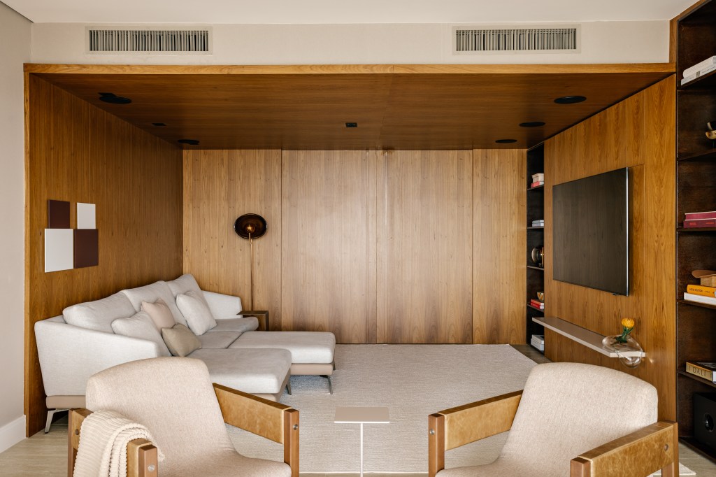 Ripado triangular veste o teto da sala deste apartamento de 450 m². Projeto de Nildo José. Na foto, sala de TV com paredes de madeira e portas embutidas.