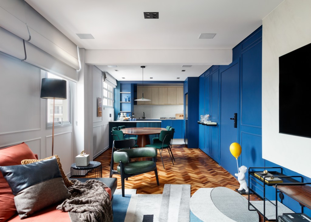 Rústico, retrô e contemporâneo: apê de 72 m² ganha vida com cozinha azul. Projeto de Ricardo Abreu. Na foto, sala com cozinha integrada, paredes de marcenaria azul e piso de espinha de peixe.