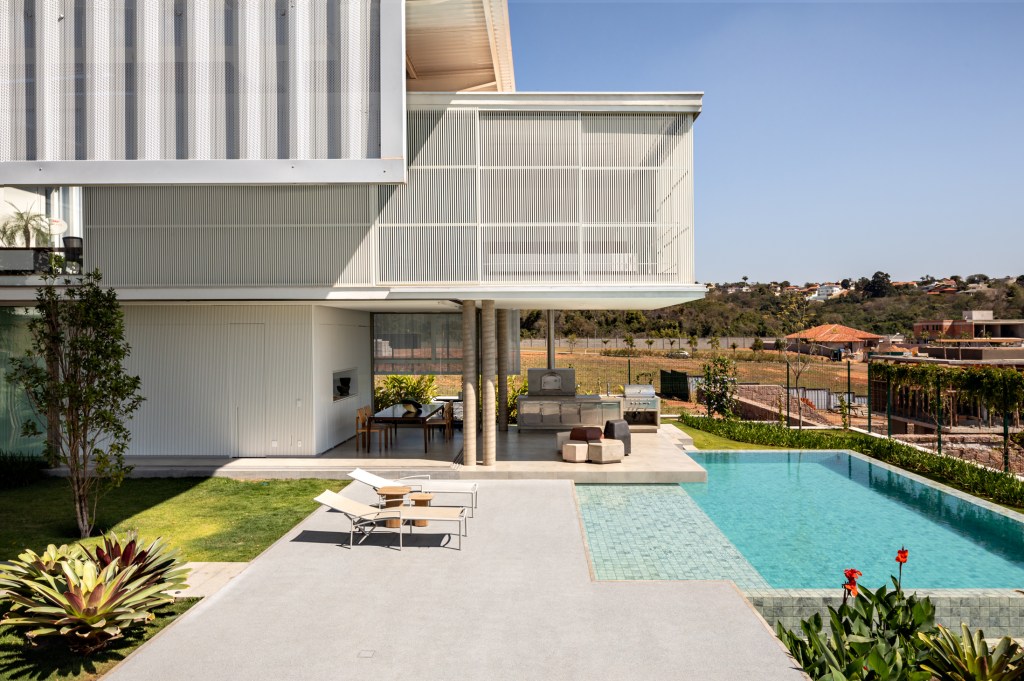 Treliças brancas de metal compõem a fachada desta casa em Campinas. Projeto de FGMF. Na foto, fachada com piscina e jardim.
