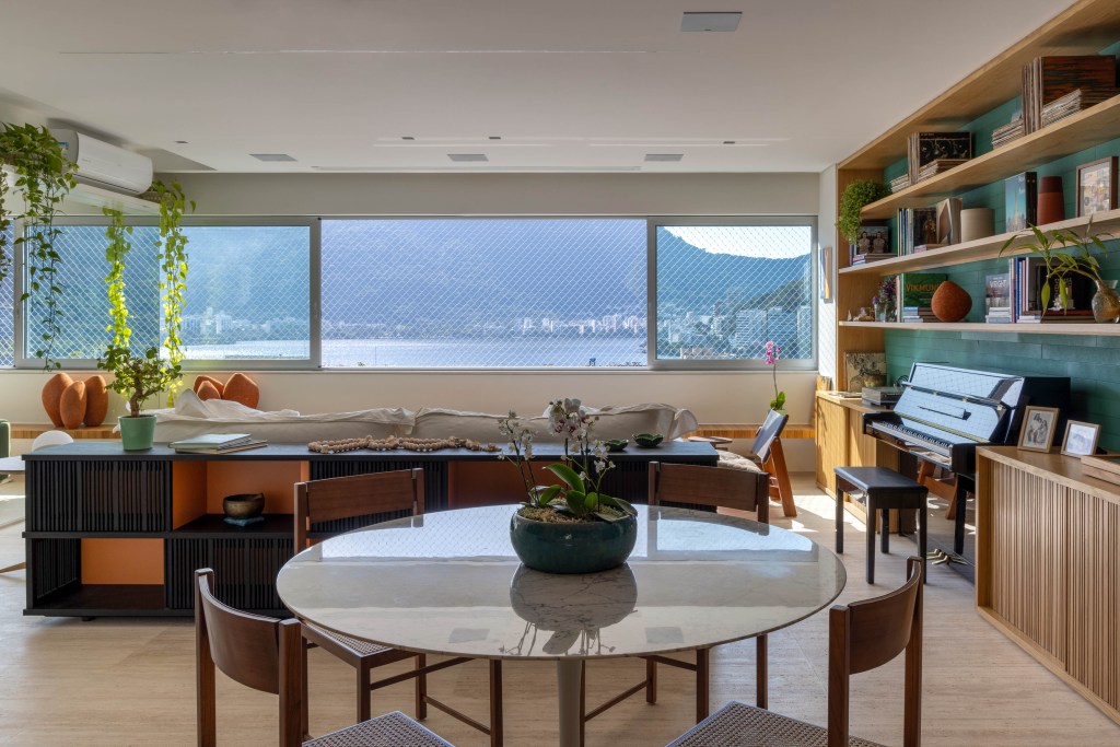 A vista para a Lagoa é o pano de fundo dos ambientes deste apê de 150 m². Projeto de Joaquim Meyer. Na foto, sala de estar com piano e parede verde. Sala de jantar com mesa redonda.