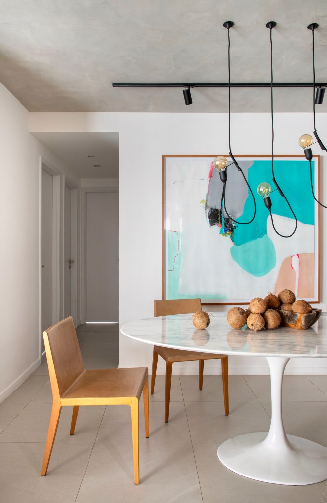 Apê de 105 m² para mãe e filha tem dois espaços de estar e cozinha gourmet. Projeto de Rafael Ramos. Na foto, sala de jantar com mesa oval, cadeiras de madeira, luminária e buffet.