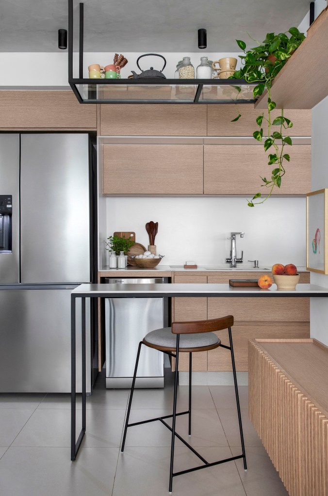 Apê de 105 m² para mãe e filha tem dois espaços de estar e cozinha gourmet. Projeto de Rafael Ramos. Na foto, cozinha integrada com bancada para refeições, armários em tom madeira.
