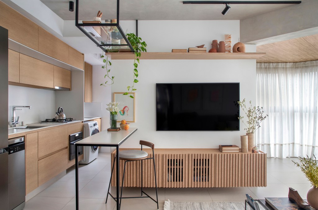 Apê de 105 m² para mãe e filha tem dois espaços de estar e cozinha gourmet. Projeto de Rafael Ramos. Na foto, sala integrada com cozinha, tv, rack ripado.