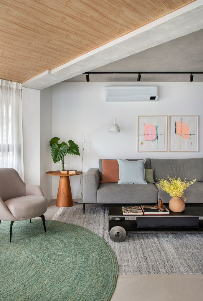 Apê de 105 m² para mãe e filha tem dois espaços de estar e cozinha gourmet. Projeto de Rafael Ramos. Na foto, sala de estar com sofá cinza, tapete verde redondo, trilho de spot.