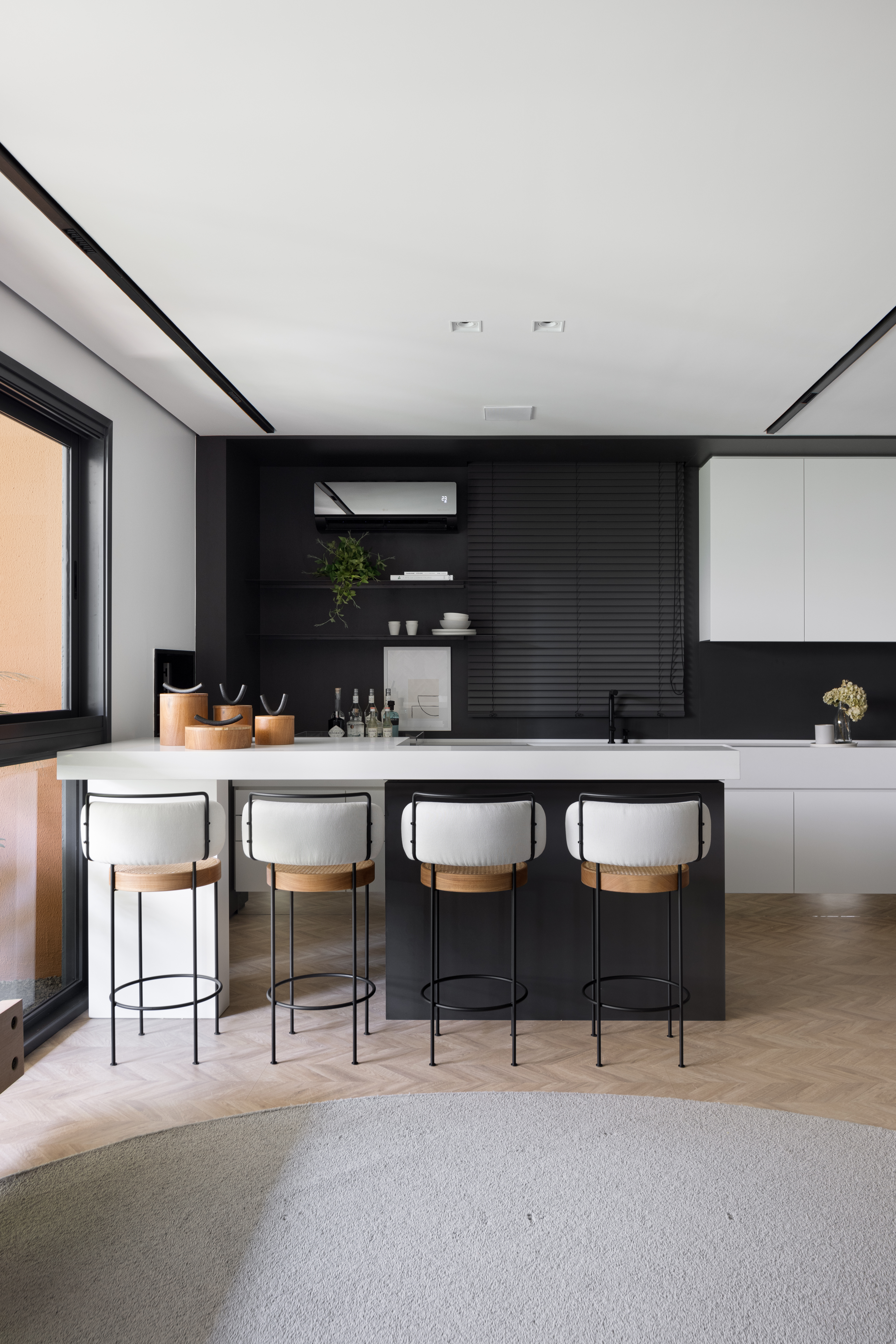 Apê de 142 m² tem paleta elegante de preto e branco e layout integrado. Projeto de Boher Arquitetos. Na foto, cozinha com parede preta, marcenaria branca, banquetas, piso de madeira.