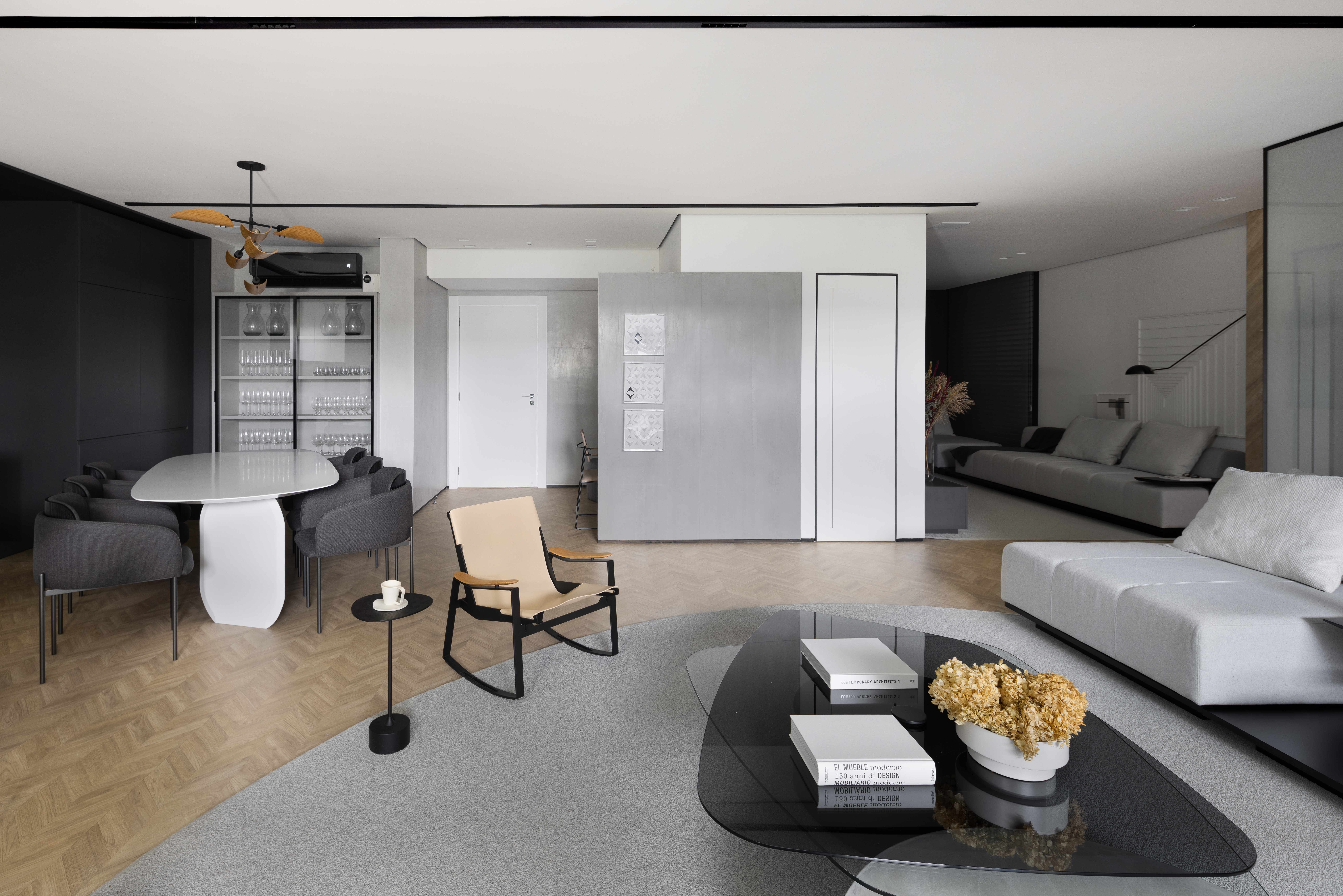 Apê de 142 m² tem paleta elegante de preto e branco e layout integrado. Projeto de Boher Arquitetos. Na foto, sala de estar com sofá cinza, mesa de centro preta, poltrona, tapete cinza.