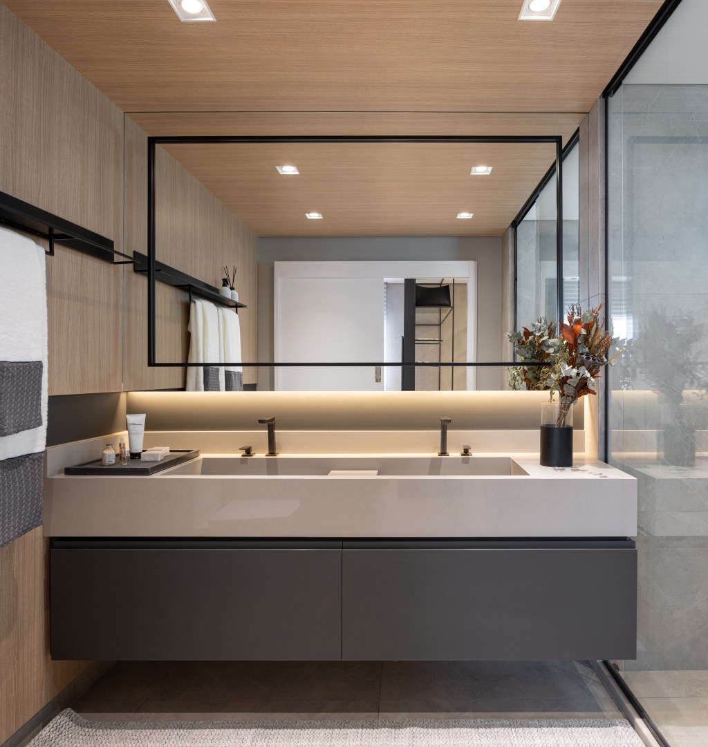 Apê de 142 m² tem paleta elegante de preto e branco e layout integrado. Projeto de Boher Arquitetos. Na foto, banheiro com cuba dupla esculpida, paredes revestidas com painéis de madeira.