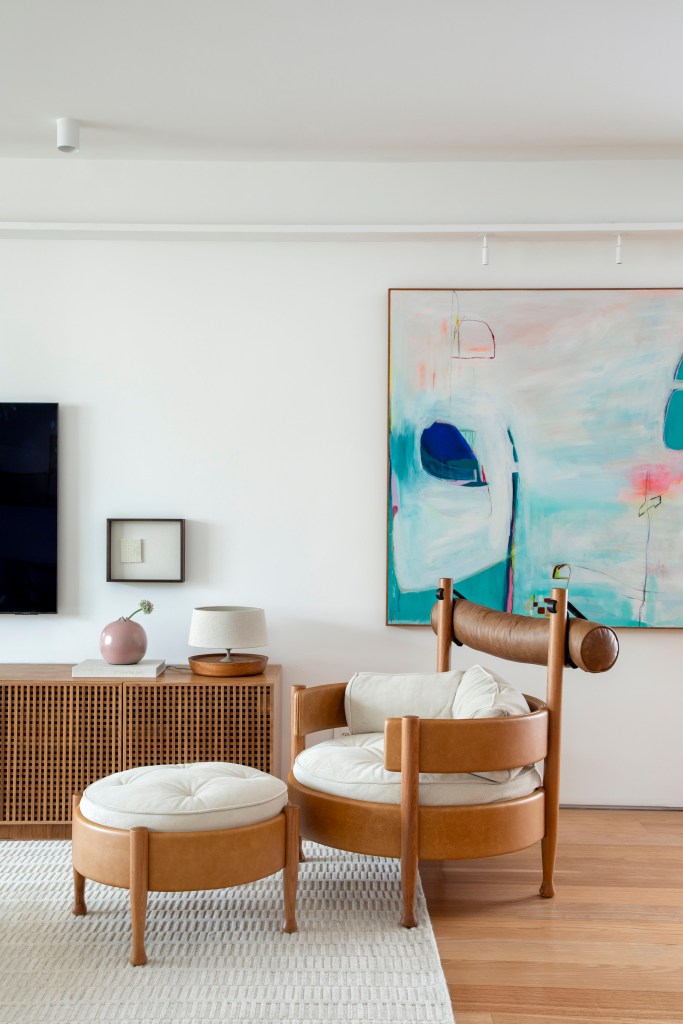 Apê de 180 m² com sala íntima equilibra minimalismo e conforto. Projeto de Studio LAK. Na foto, sala de estar neutra, poltrona vivi com pufe, rack de madeira.