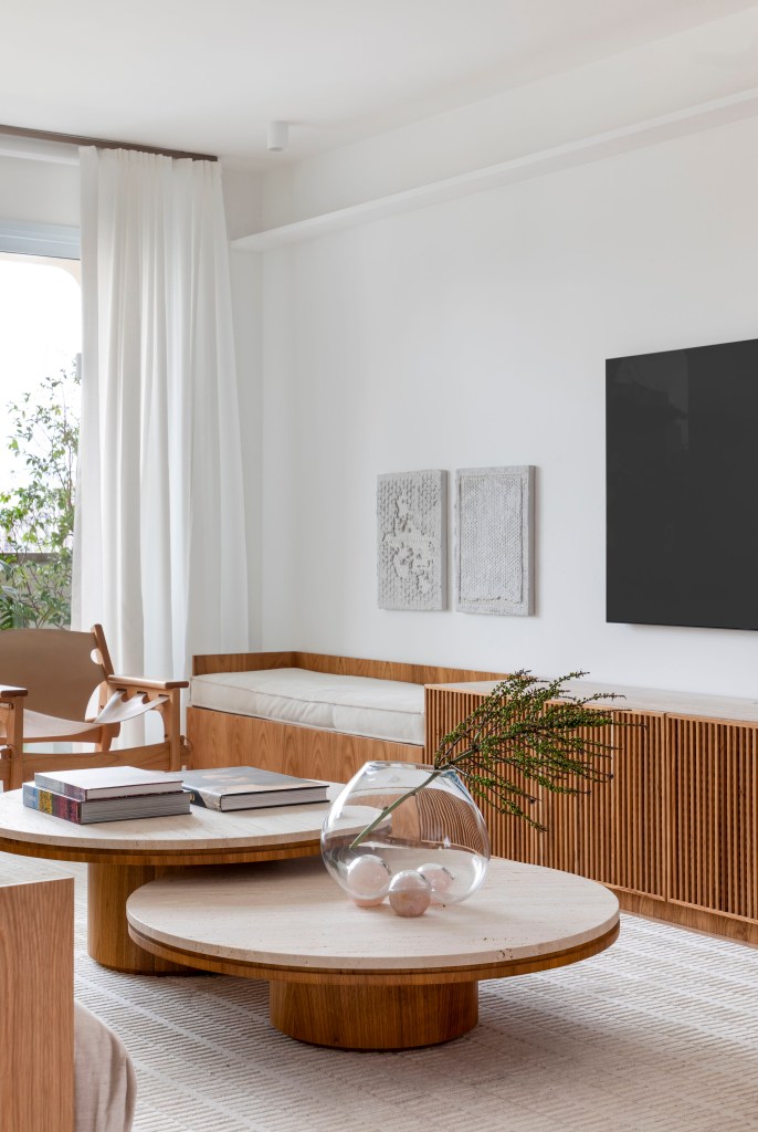 Apê de 180 m² com sala íntima equilibra minimalismo e conforto. Projeto de Studio LAK. Na foto, sala de estar neutra, tv, rack ripado, mesa de centro.
