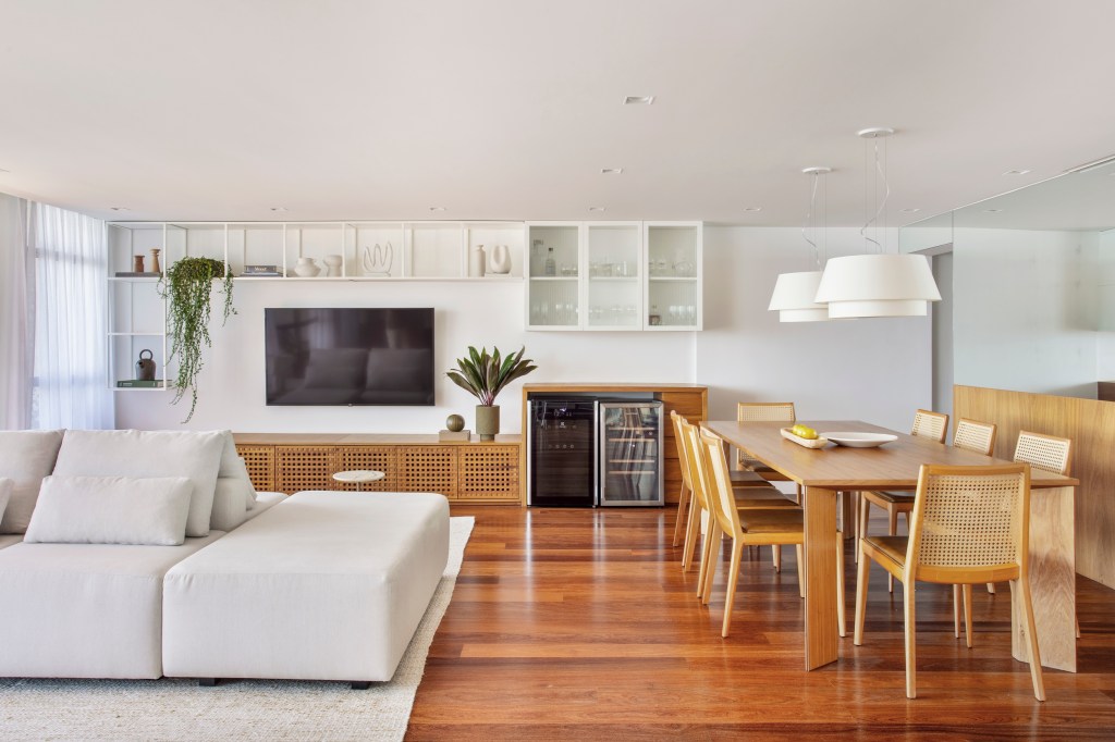 Apê de 300 m² tem sala íntima com TV e cozinha com armários amarelos. Projeto de PKB Arquitetura. Na foto, sala de estar integrada com sala de jantar, piso de madeira.